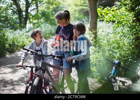 Mère et fils buvant de l'eau sur une promenade en vélo dans un parc ensoleillé Banque D'Images