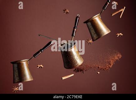 Vieilles cafetières en cuivre et une cuillère avec café moulu en mouvement. Café moulu renversé, haricots, cannelle et anis en mouvement. Arrière-plan marron. Copier Banque D'Images