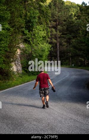 Un photographe de randonnée explore une route de montagne, pour la chasse photographique des animaux sauvages. L'homme tient un appareil photo reflex avec objectif et bouteille d'eau. Banque D'Images