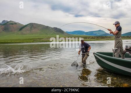 Un pêcheur de mouche avec une truite de Taimen au bout de sa ligne d'un bateau, sur le fleuve Delger Moron en Mongolie, Moron, Mongolie - 14 juillet 2014 Banque D'Images