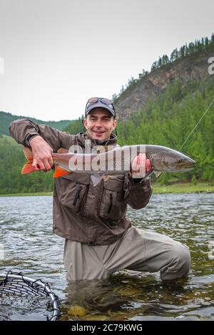 Pêcheur de mouche portant fièrement une truite taimen, pêchée sur le fleuve Delger Moron en Mongolie, Moron, Mongolie - 14 juillet 2014 Banque D'Images