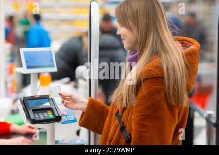 La jeune femme avec une carte de crédit paie pour les achats au comptoir de caisse du magasin Banque D'Images