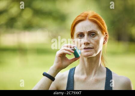 Portrait d'une femme mûre à l'estime sérieuse utilisant un inhalateur pour prévenir l'asthme attaque après l'entraînement dans le parc Banque D'Images