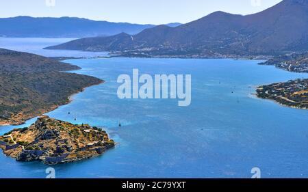 Vue sur le port entre l'île et la péninsule de Spinalonga, connue sous le nom de Kalydon, et le village de Plaka d'en haut, Crète, Grèce. Banque D'Images