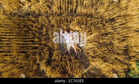 Vue de drone à une jeune famille heureuse couché et reposant au milieu du champ de blé jaune avec bébé. Banque D'Images