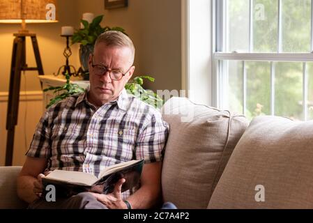 Un homme est assis seul, à l'intérieur, à lire un grand livre. Banque D'Images