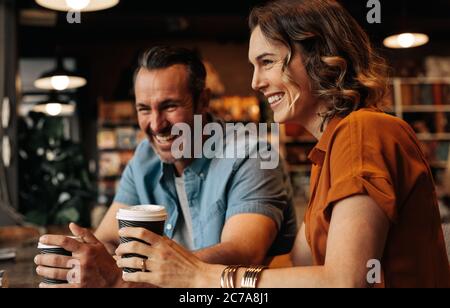 Couple joyeux assis au café ayant un café. Homme et femme assis à la table du restaurant souriant tout en prenant un café. Banque D'Images