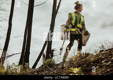 Femmes plantant des arbres dans la forêt. Femme jardinière d'arbre portant un gilet réfléchissant marchant dans un sac de transport forestier plein d'arbres et une pelle. Banque D'Images