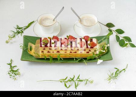 Gâteau aux fruits avec fraise, tasses de café et fleurs fraîches sur la table. Petit déjeuner romantique pour deux, plat. Banque D'Images