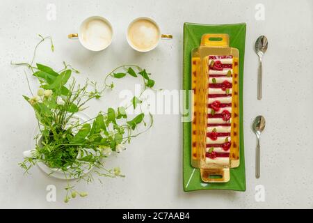 Gâteau à la crème et à la fraise, deux tasses de café et des fleurs sur une table légère. Vue de dessus, plan d'appartement. Bannière. Banque D'Images