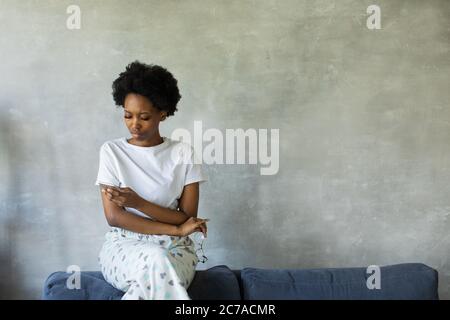 Femme afro-américaine avec visage réfléchi assis sur un canapé Banque D'Images