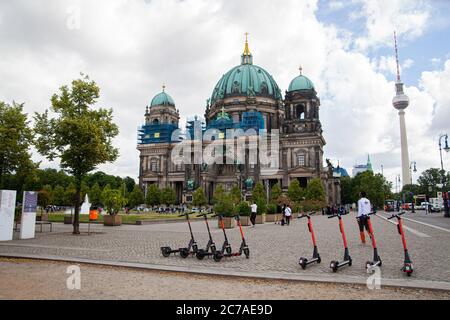 Une cathédrale de Berlin avec une tour de télévision en arrière-plan et une ligne de scooters électriques en premier plan Banque D'Images