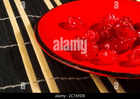 Cerises séchées sucrées dans une soucoupe rouge sur un tapis de bambou, gros plan. Banque D'Images