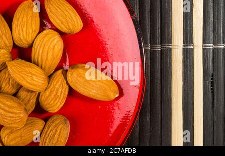Noix d'amandes dans une soucoupe rouge sur un tapis de bambou, gros plan Banque D'Images