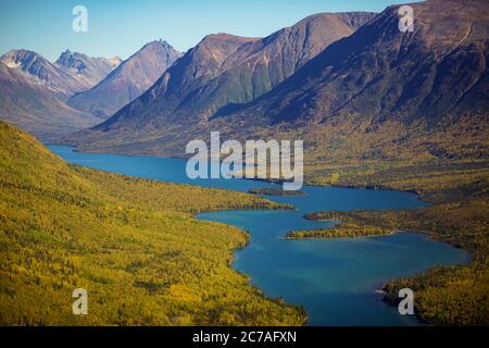 Une vue aérienne à couper le souffle d'une rivière sinueuse nichée entre des montagnes escarpées et des forêts d'automne dorées dans la nature sauvage préservée de l'Alaska. Banque D'Images