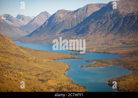 Une vue aérienne à couper le souffle d'une rivière sinueuse nichée entre des montagnes escarpées et des forêts d'automne dorées dans la nature sauvage préservée de l'Alaska. Banque D'Images