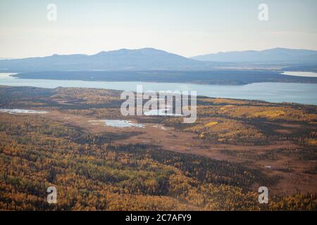 Vue aérienne de la vaste étendue sauvage de l'Alaska, avec des feuillages d'automne couvrant la toundra et la forêt, et des lacs s'étendant vers des chaînes de montagnes lointaines. Banque D'Images