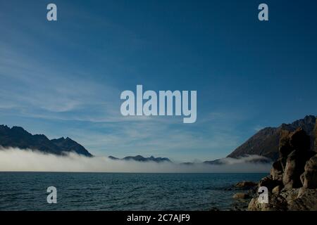 Le brouillard roule sur les eaux du lac Iliamna, en Alaska, avec le soleil projetant la lumière sur la silhouette accidentée de la montagne et le paysage sauvage serein Banque D'Images