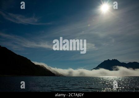 Le brouillard roule sur les eaux du lac Iliamna, en Alaska, avec le soleil projetant la lumière sur la silhouette accidentée de la montagne et le paysage sauvage serein Banque D'Images