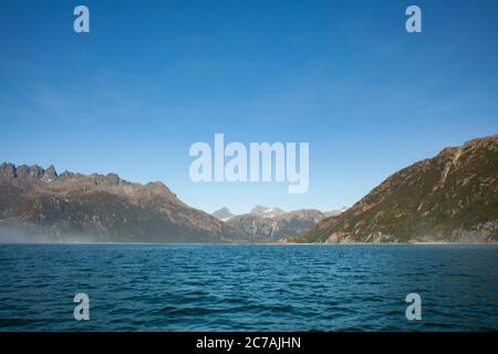 Le brouillard roule sur les eaux du lac Iliamna, en Alaska, avec le soleil projetant la lumière sur la silhouette accidentée de la montagne et le paysage sauvage serein Banque D'Images