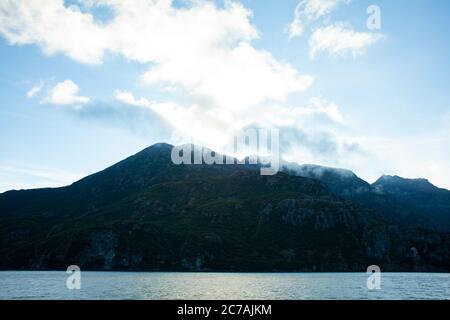 Le brouillard roule sur les eaux du lac Iliamna, en Alaska, avec le soleil projetant la lumière sur la silhouette accidentée de la montagne et le paysage sauvage serein Banque D'Images