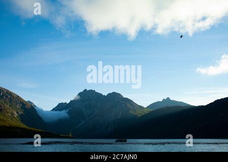 Le brouillard roule sur les eaux du lac Iliamna, en Alaska, avec le soleil projetant la lumière sur la silhouette accidentée de la montagne et le paysage sauvage serein Banque D'Images