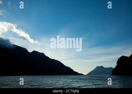 Le brouillard roule sur les eaux du lac Iliamna, en Alaska, avec le soleil projetant la lumière sur la silhouette accidentée de la montagne et le paysage sauvage serein Banque D'Images