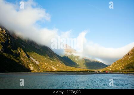 Des nuages brumeux roulent sur les pentes accidentées des montagnes entourant une vallée sereine du lac en Alaska, mettant en valeur sa beauté intacte. Banque D'Images