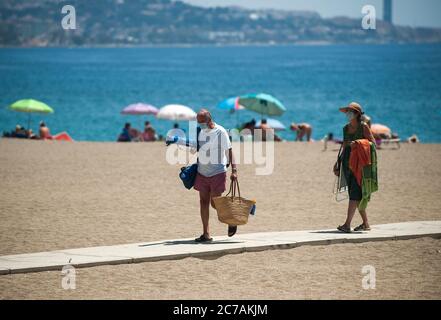 Malaga, Espagne. 15 juillet 2020. Un couple portant des masques de visage se promo le long de la plage de Malagueta pendant la première journée d'utilisation obligatoire des masques de visage.de nouvelles infections à coronavirus en Espagne après l'assouplissement des restrictions ont amené le gouvernement régional à imposer l'utilisation obligatoire des masques de visage en plein air et les lieux fermés et les plages, même lorsqu'ils observent une distance de sécurité entre les personnes. Cette mesure vise à freiner la propagation de la pandémie du coronavirus. Crédit: Jesus Merida/SOPA Images/ZUMA Wire/Alay Live News Banque D'Images