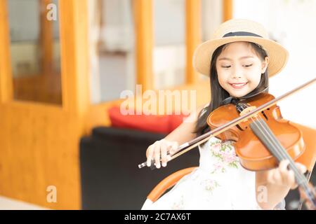 Une mignonne fille d'école élémentaire asiatique joue un violon heureusement dans sa maison. Banque D'Images