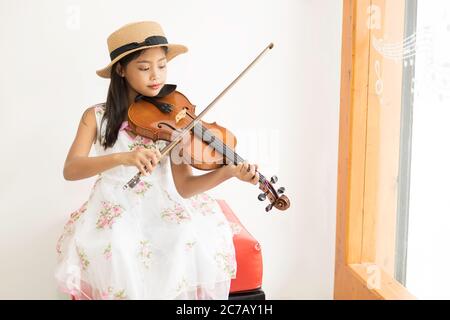 Une mignonne fille d'école élémentaire asiatique joue un violon heureusement dans sa maison. Banque D'Images