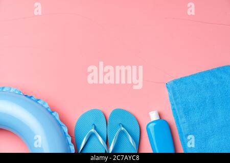 Concept de plage avec anneau en caoutchouc bleu, serviette, tongs et humidifiant sur fond rose Banque D'Images