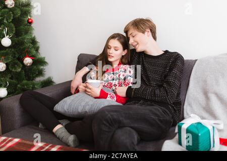 Jeune beau couple assis sur un canapé à la maison et passer du temps avec l'arbre de Noël près Banque D'Images