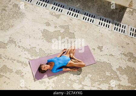 Une jeune femme allongé sur un tapis de yoga et s'entraîne à poser du yoga tout en fermant les yeux de manière réfléchie Banque D'Images