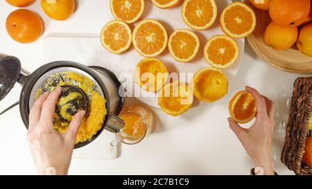 Jus d'orange fraîchement pressé. Femme caucasienne pressant les oranges à l'aide d'une centrifugeuse électrique. Gros plan sur fond blanc, vue du dessus Banque D'Images