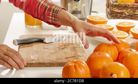 La femme coupe des oranges sur une planche de cuisine en bois avec fond blanc. Préparation du jus d'orange frais à l'aide d'une centrifugeuse électrique. Banque D'Images