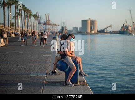 Malaga, Espagne. 15 juillet 2020. Un couple portant des masques de visage vu embrassant à la promenade de la promenade 'Muelle Uno' pendant le premier jour de l'utilisation obligatoire des masques de visage. De nouvelles infections à coronavirus en Espagne après l'assouplissement des restrictions ont amené le gouvernement régional à imposer l'utilisation obligatoire de masques faciaux en plein air et dans les lieux fermés et les plages, même lorsqu'ils observent une distance de sécurité entre les gens. Cette mesure vise à freiner la propagation de la pandémie du coronavirus. Crédit : SOPA Images Limited/Alamy Live News Banque D'Images