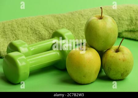 Cloches en plastique près de la pyramide des pommes vertes juteuses. Équipement sportif et de santé, gros plan. Athlétisme et concept de perte de poids. Haltères de couleur vert vif, serviette et fruits sur fond vert Banque D'Images