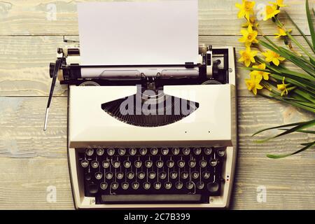 ancienne machine à écrire ancienne vintage avec papier et fleurs jaunes printanières sur fond en bois, joyeuses pâques, femme ou fête des mères, travail de bureau, lettre romantique d'amour, alphabet et clavier Banque D'Images