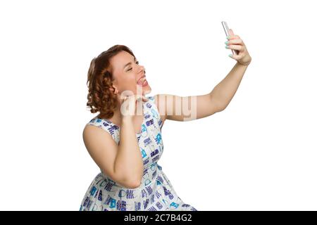 Portrait d'une jeune fille en surpoids à tête rouge sur un fond blanc isolé. Photographié en profil, se berner et montrer sa langue tout en prenant un selfie Banque D'Images