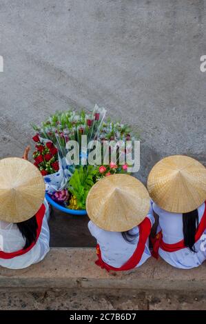 Les femmes portant des robes traditionnelles (Ao Dai) et des chapeaux de cône (non la) assis dans le port de qui Nhon dans le centre du Vietnam attendant d'accueillir les touristes de Banque D'Images