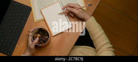 Photo de tête de carnet de notes de journal écrit féminin sur la table d'étude avec une tasse à café, une tablette et un livre Banque D'Images