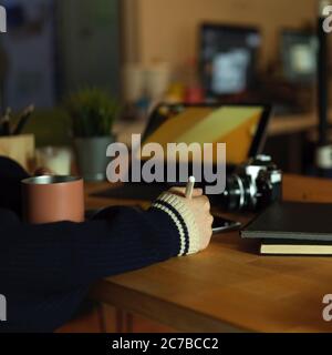 Photo rognée d'une graphiste féminine travaillant avec une tablette numérique sur une table de travail rustique avec un appareil photo, une tasse et des fournitures Banque D'Images