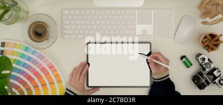 Vue de dessus d'une femme de créateur travaillant avec une tablette, un ordinateur, un appareil photo et des fournitures sur un bureau blanc Banque D'Images