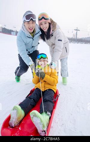 Parents de ski poussant un fils assis dans la glissade de neige Banque D'Images