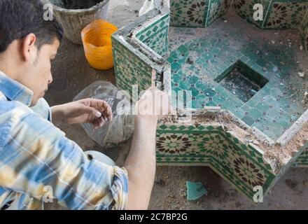 Homme marocain travaillant sur une mosaïque de décoration dans une poterie à Fès, Maroc. Banque D'Images