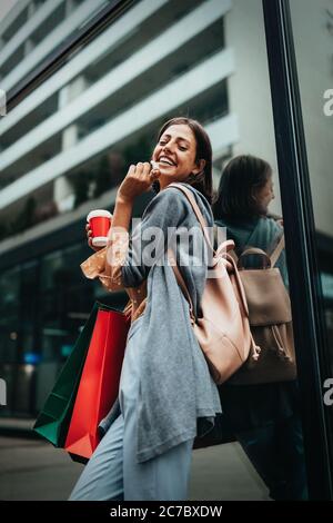 Une jeune femme heureuse à boire du café et à marcher avec des sacs après avoir fait du shopping en ville. Banque D'Images