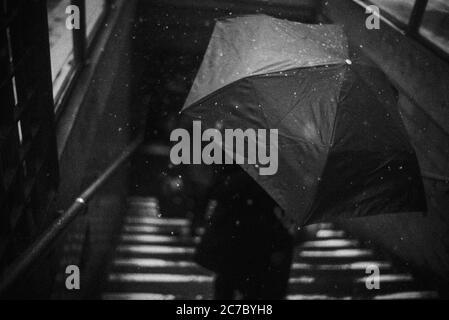 Gros plan prise de vue en niveaux de gris grand angle d'une personne qui détient un Grand parasol sur l'escalier en hiver Banque D'Images