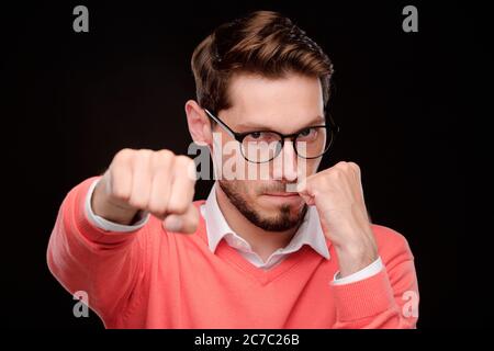Portrait d'un jeune homme sérieux et confiant dans des lunettes de vue qui jette un coup de poing tout en se protégeant Banque D'Images