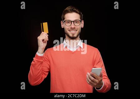 Portrait d'un jeune homme souriant dans des lunettes à l'aide de l'application pour smartphone tout en vérifiant le solde de la carte de crédit Banque D'Images